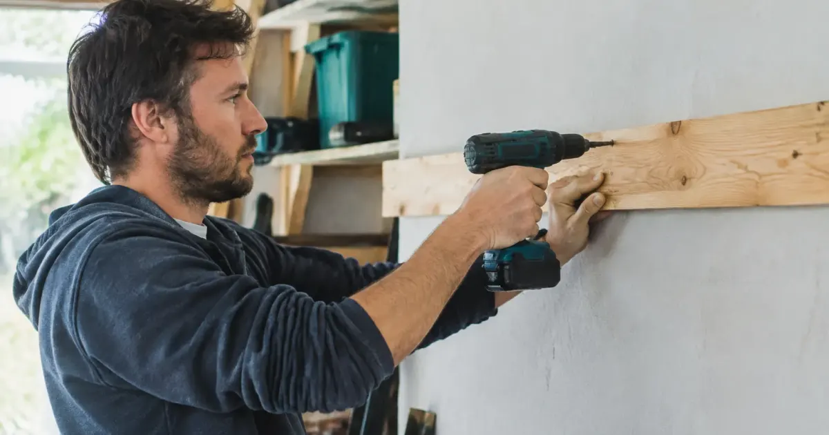 Un bricoleur visse une planche bois horizontale au mur
