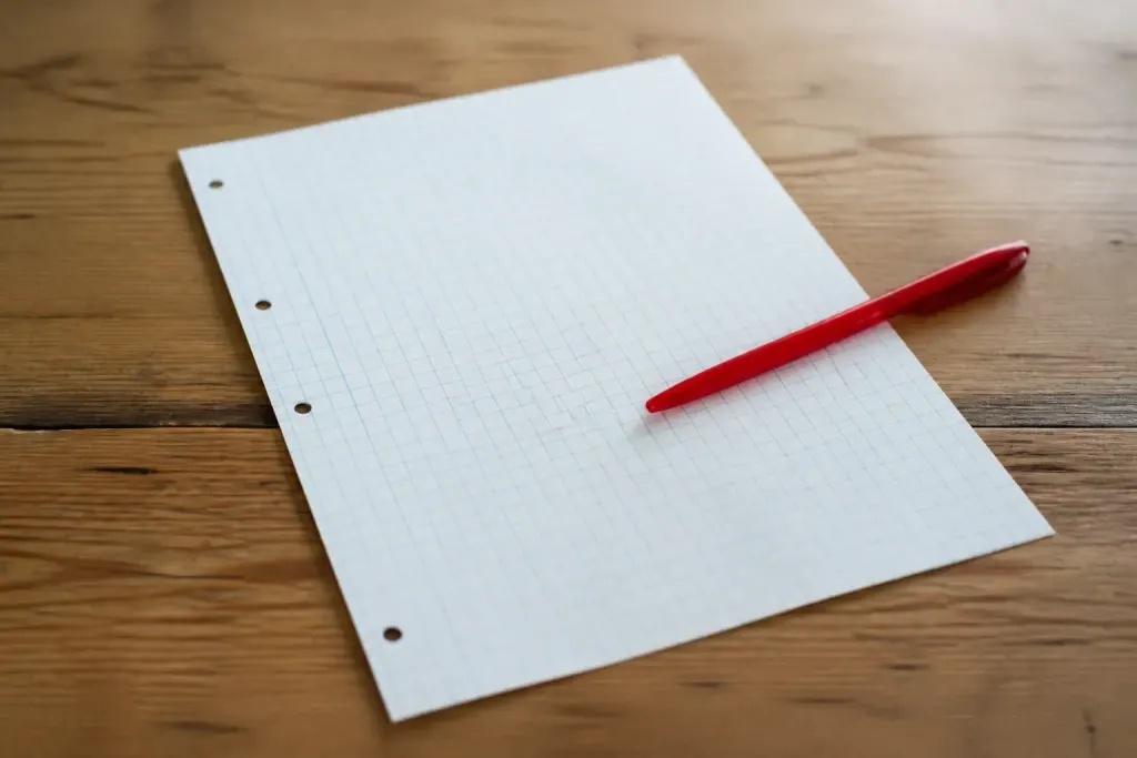 Feuille quadrillee posee sur un bureau avec stylo rouge