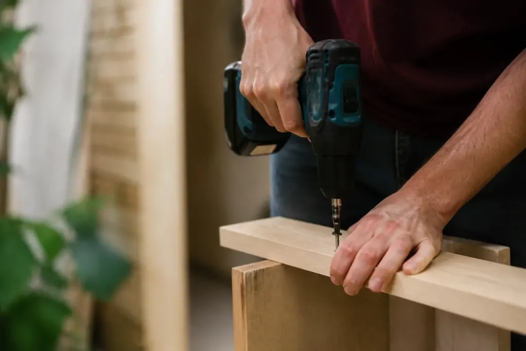 Mains vissant une planche de bois, perceuse sans fil
